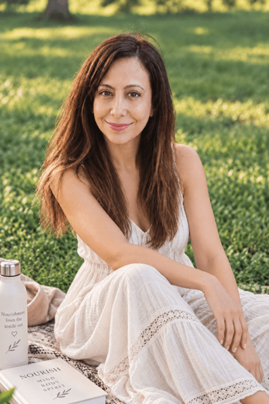 Anna Almiroudis sitting on the grass in a white dress with a water bottle and book